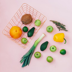 Basket with green fruits and vegetables on pastel pink background