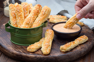 Homemade savory bread sticks with cheese and sesame in a basket, served with sauce on wooden board, horizontal