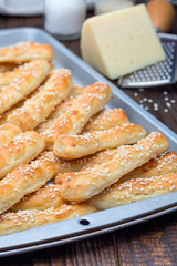 Homemade savory bread sticks with cheese and sesame on baking tray, vertical