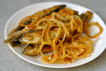 Fried fish and fried onions on a white dish. Close-up