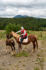 A man rides a horse, a foal walks beside him and interferes under his feet.