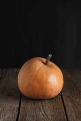 Pumpkin on a rustic wood table on dark background. Front view. Copy space.