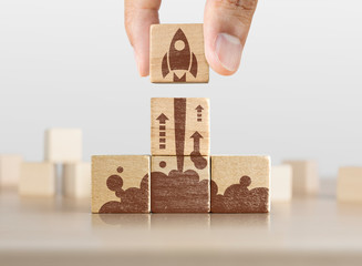 Business start up, start, new project or new idea concept. Wooden blocks with launching rocket graphic arranged in pyramid shape and a man is holding the top one. - obrazy, fototapety, plakaty