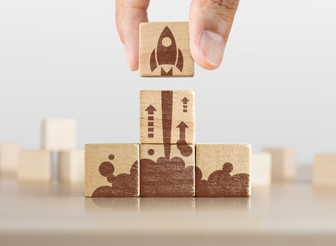 Business start up, start, new project or new idea concept. Wooden blocks with launching rocket graphic arranged in pyramid shape and a man is holding the top one.