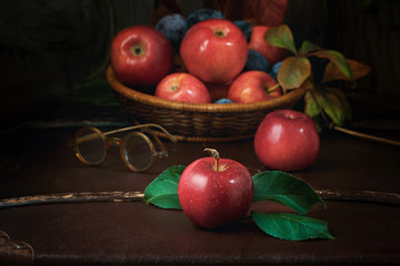 Red apples, plums, eyeglasses on a vintage suitcase