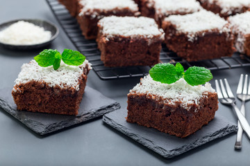 Fototapeta na wymiar Homemade brownie with coconut flakes, swedish dessert Karleksmums, cut in square servings, on stone plate, horizontal