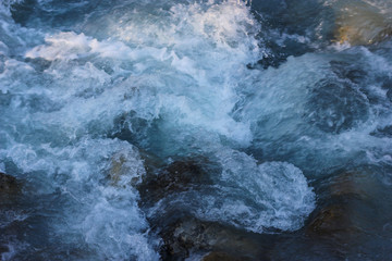 Close up of bright blue flowing water stream of mountain river with stony banks in in the Alps, Chamonix. Atmospheric dynamic background