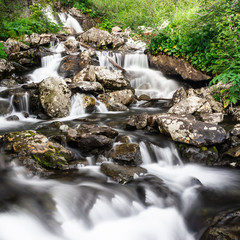 Waterfall in mountains. Rapid flow in river. Water in rocks, trip along river.