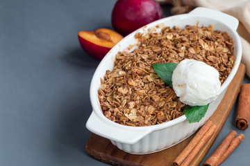 Plum crumble pie or plum crisp with oats and spices, served with vanilla ice cream ball, in baking dish, horizontal, copy space