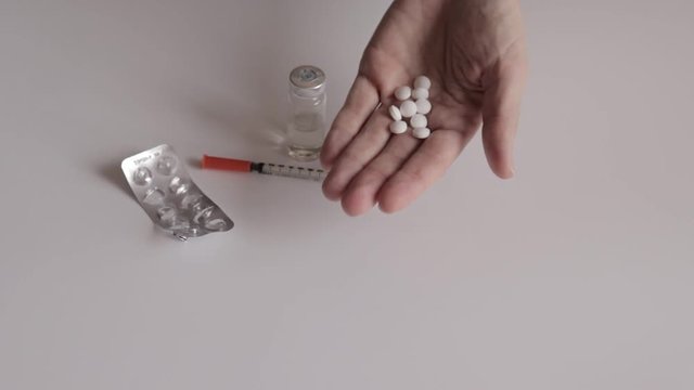 A woman showing white tablets in hand and throwing it down - empty blister, siringe and vial on white table background