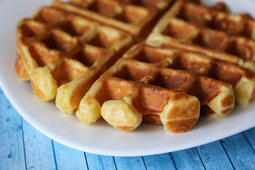Belgian waffles in white plate on wooden table. Tasty breakfast closeup, freshly baked classic wafer