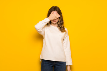 Teenager girl over yellow wall covering eyes by hands. Do not want to see something