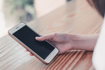 Croppes shot women hand holding white smartphone with blank screen on wooden counter bar in cafe. vintage tone for business technology background concept. closeup mobile.