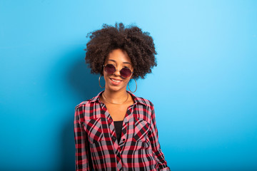 Fototapeta na wymiar Cheerful attractive afro brazilian girl enjoying life wearing sunglasses On blue wall background - Imagem
