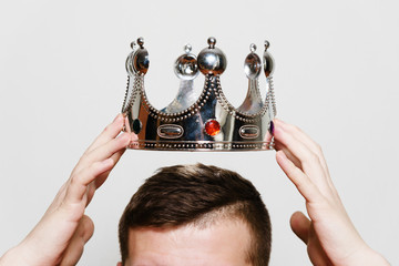 Man hands holding crown over his head, on light gray background, in studio.