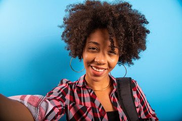 Closeup portrait of smiling young attractive African brazilian woman holding smartphone, taking selfie photo on the blue background
