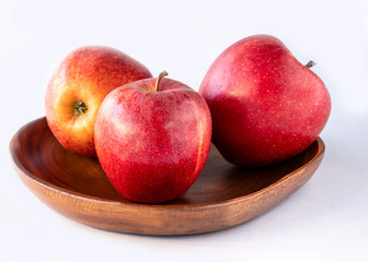Three red apples on the wooden plate and white background