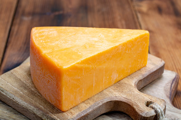 Piece of bright yellow hard cheese cheddar, originating in the English village of Cheddar in Somerset