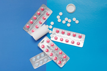 Blisters rose capsule and white round tablets on blue background, medical pharmacy concept
