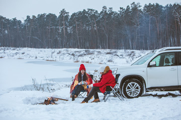 man with woman sitting on chairs near camp fire in winter time. car travel.