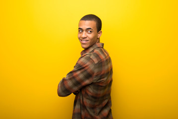 Young african american man on vibrant yellow background looking over the shoulder with a smile