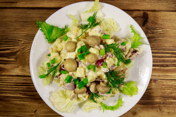 Potato salad with marinated mushrooms, eggs, red onion and mayonnaise on wooden table