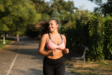 Young beautiful smiling plus size woman in sporty top and leggings joyfully looking aside while...