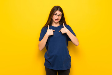 Young woman with glasses over yellow wall with surprise facial expression