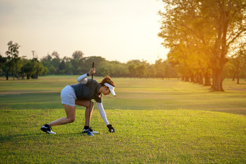 Sporty asian golfer woman putting golf ball on tee with club in golf course on sunny day for...
