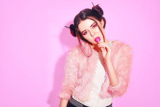 Girl in pink with win buns eats Chupa Chups. Portrait of a pretty young girl eating lollipop over pink background.  Lovely smiling teenage girl eating sweets. Health, people, food, diet.