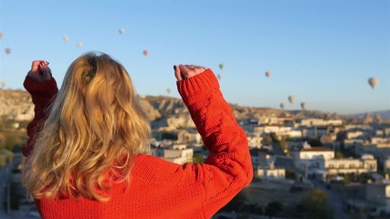 happy woman raising hands with a view of the Cappadocia balloons