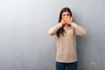 Teenager girl with sweater on a vintage wall covering mouth with hands for saying something inappropriate