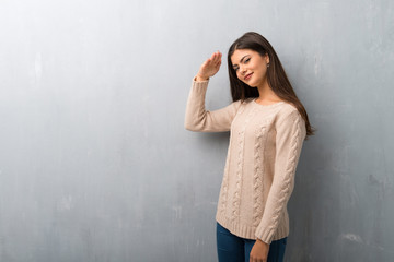 Teenager girl with sweater on a vintage wall saluting with hand