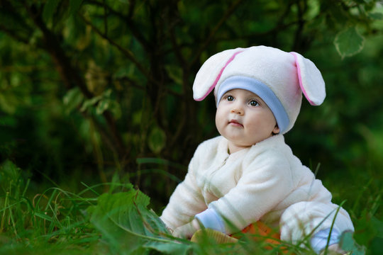 Little girl in bunny costume seating on grass in forest.