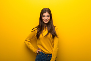 Fototapeta premium Teenager girl on vibrant yellow background posing with arms at hip and smiling