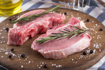 Raw pork meat on a wooden board with rosemary. Closeup