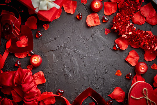 Love and Valentines day concept. Red roses petals, candles, dating accessories, boxed gifts, hearts, sequins on black stone background, frame composition, top view. Layout for greeting card