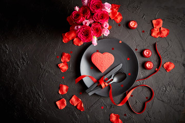 Valentines day, table setting and romantic dinner concept. Close up of plate with cutlery and rose petals on black stone background