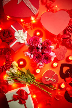Valentines day romantic decoration with roses, boxed gifts, candles, on a red background table. Top view, copy space.
