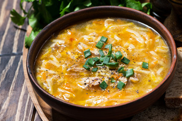 chicken soup with egg noodles in a bowl on wooden background, closeup
