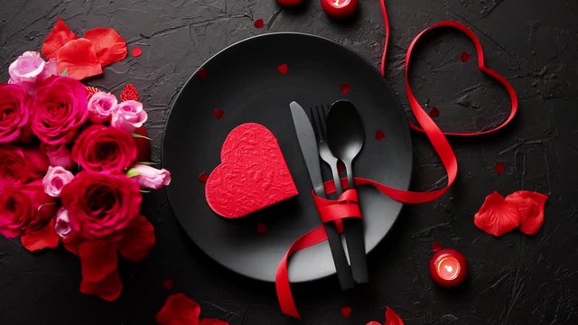 Valentines day, table setting and romantic dinner concept. Close up of plate with cutlery and rose petals on black stone background