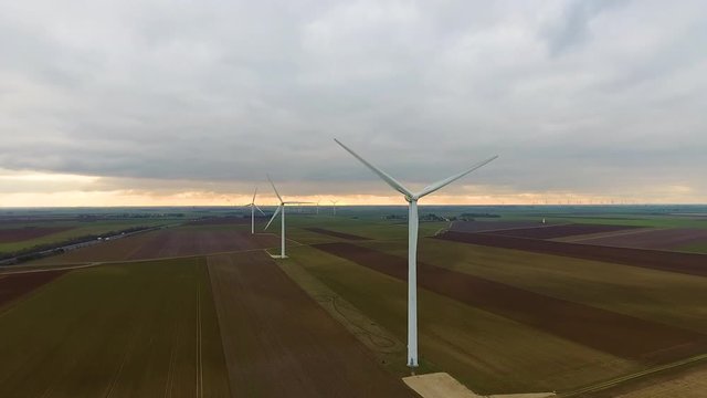 Aerial back tracking over wind turbines in crop fields during sunset France