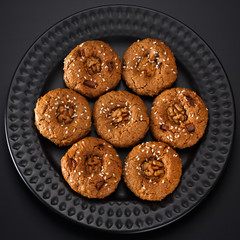 Homemade oatmeal cookies with nuts, chocolate chips and sesame. On a black plate.  View from above.