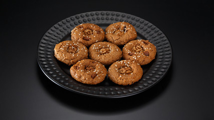 Homemade oatmeal cookies with nuts, chocolate chips and sesame. On a black plate.