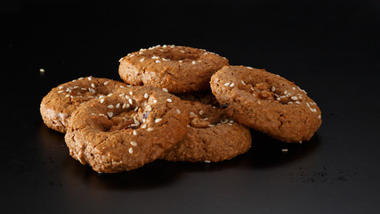 A bunch of homemade oatmeal cookies with nuts, chocolate chips and sesame. On a black background.