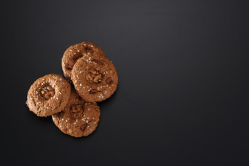 A bunch of homemade oatmeal cookies with nuts, chocolate chips and sesame. On a black background. View from above.