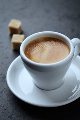 Cup of coffee and two brown sugar cubes on black stone background. Close up. 