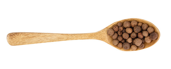 Allspices or Jamaica pepper in wooden spoon isolated on white background. Top view