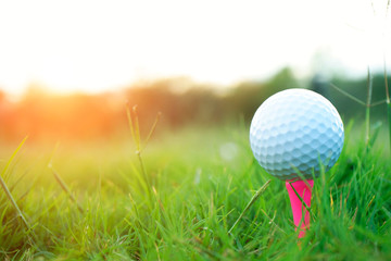 Golf ball on tee in beautiful golf course at sunset background.