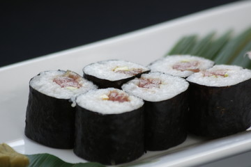 Rolls of sushi with rice nori seeweed and fish on a white plate with hashi chopsticks in a gourmet menu.